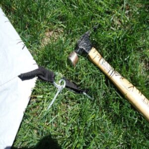 hammer laying on grass next to stakes for camping tent