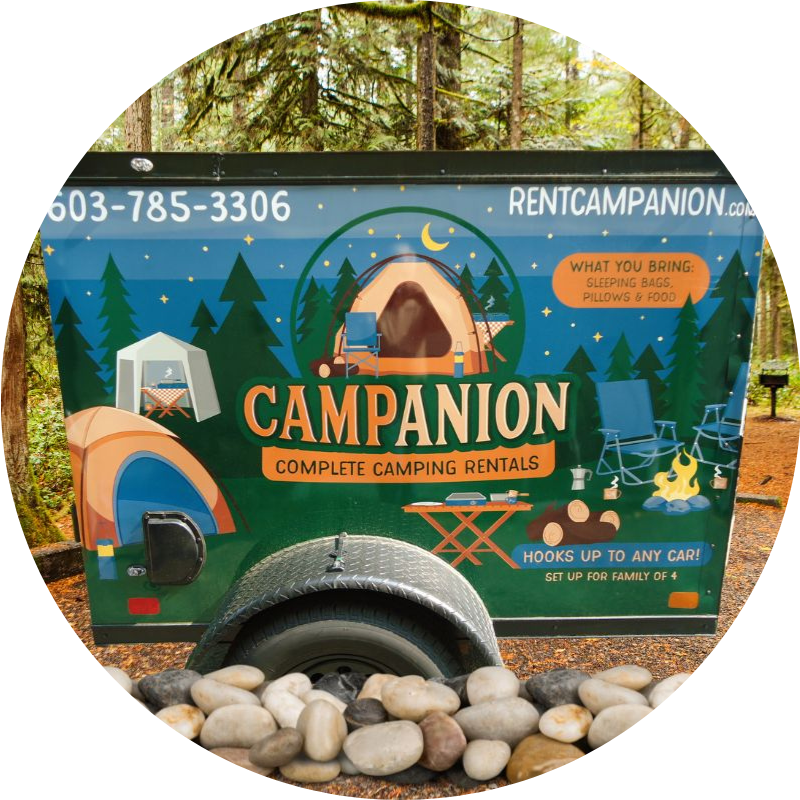Campanion camping equipment rental trailer on a campsite with rocks in front